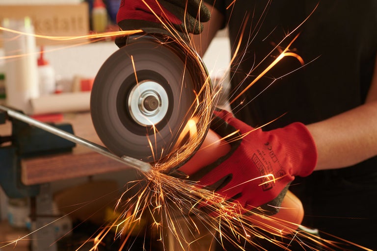 Närbild av en person som slipar metall med en vinkelslip, med gnistor som flyger