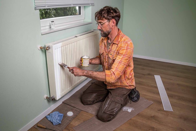 Man målar radiator med pensel och färg.