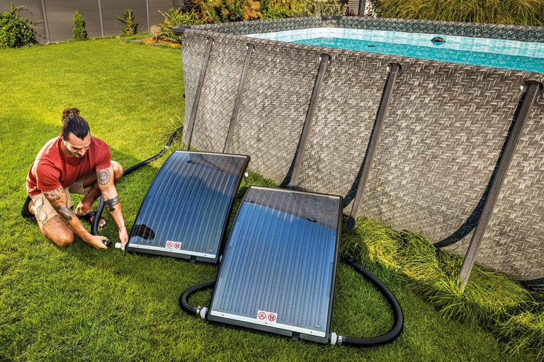 En man installerar solfångare bredvid en trädgårdspool för pooluppvärmning.