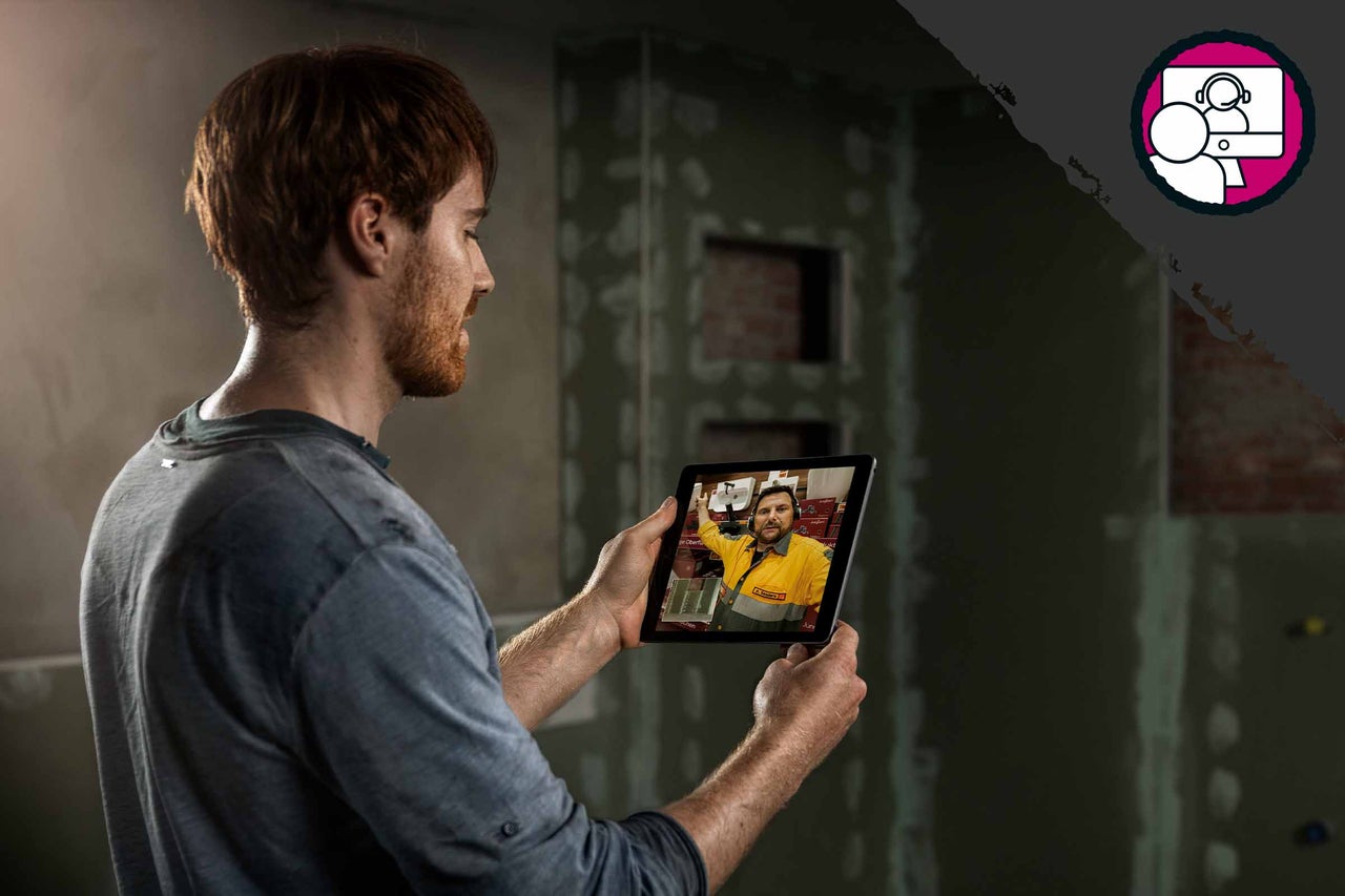 Man håller surfplatta med videosamtal framför oavslutad vägg