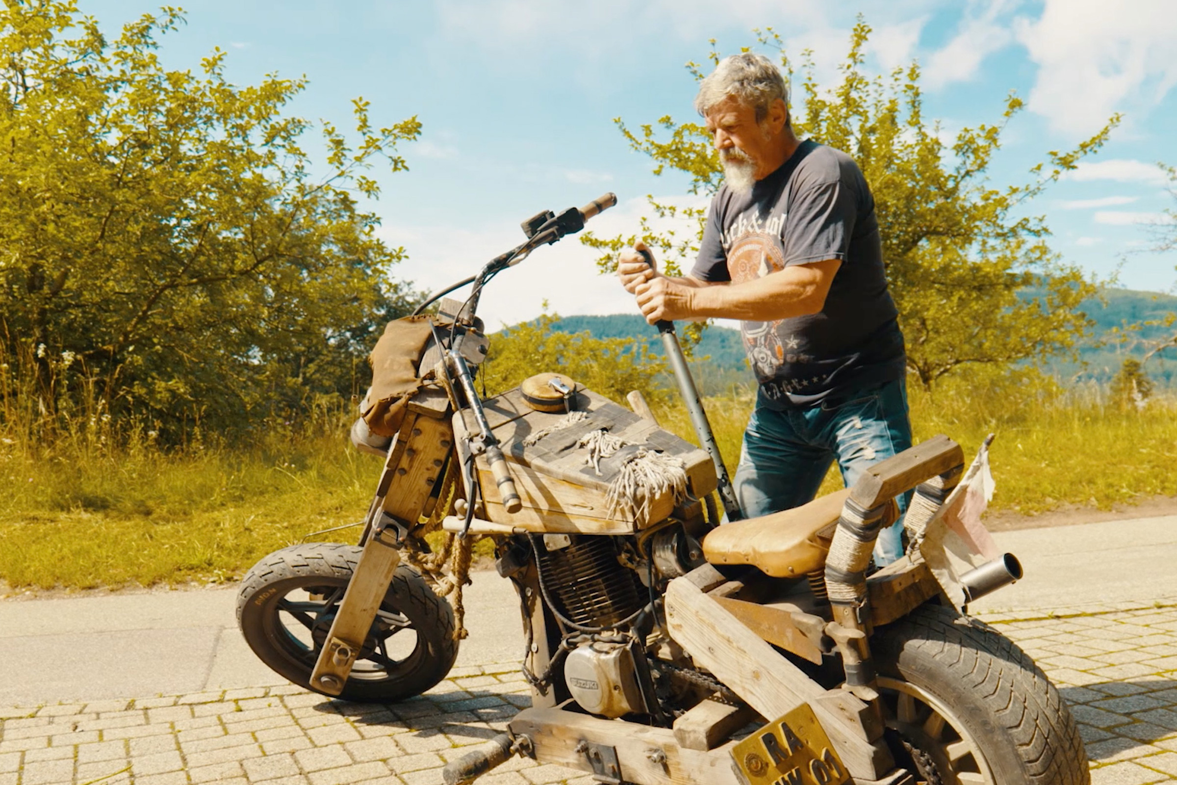 Man med motorcykel i terrängen. Motorcykeln är gjord av trä.