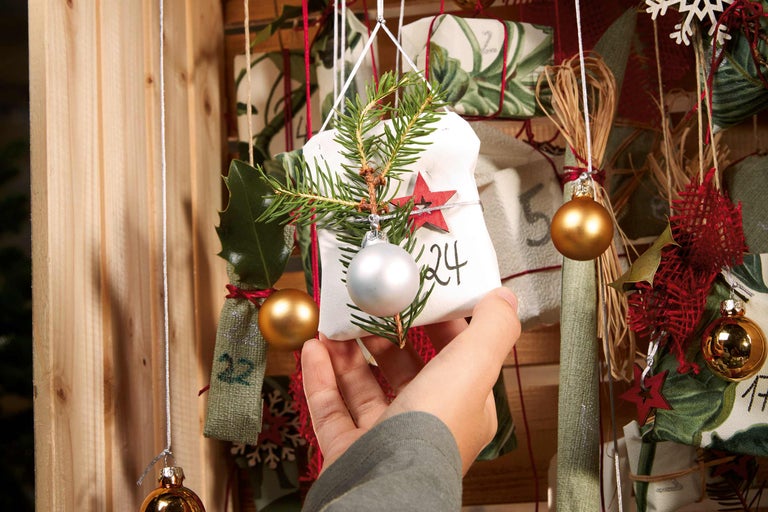 Hand öppnar fack på adventskalender med grankvist och julgranskula