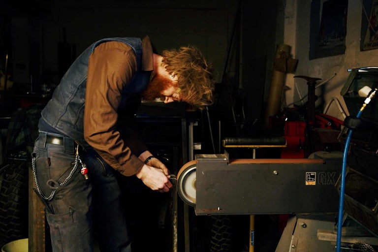 Man arbetar med en bandslipmaskin i en verkstad.
