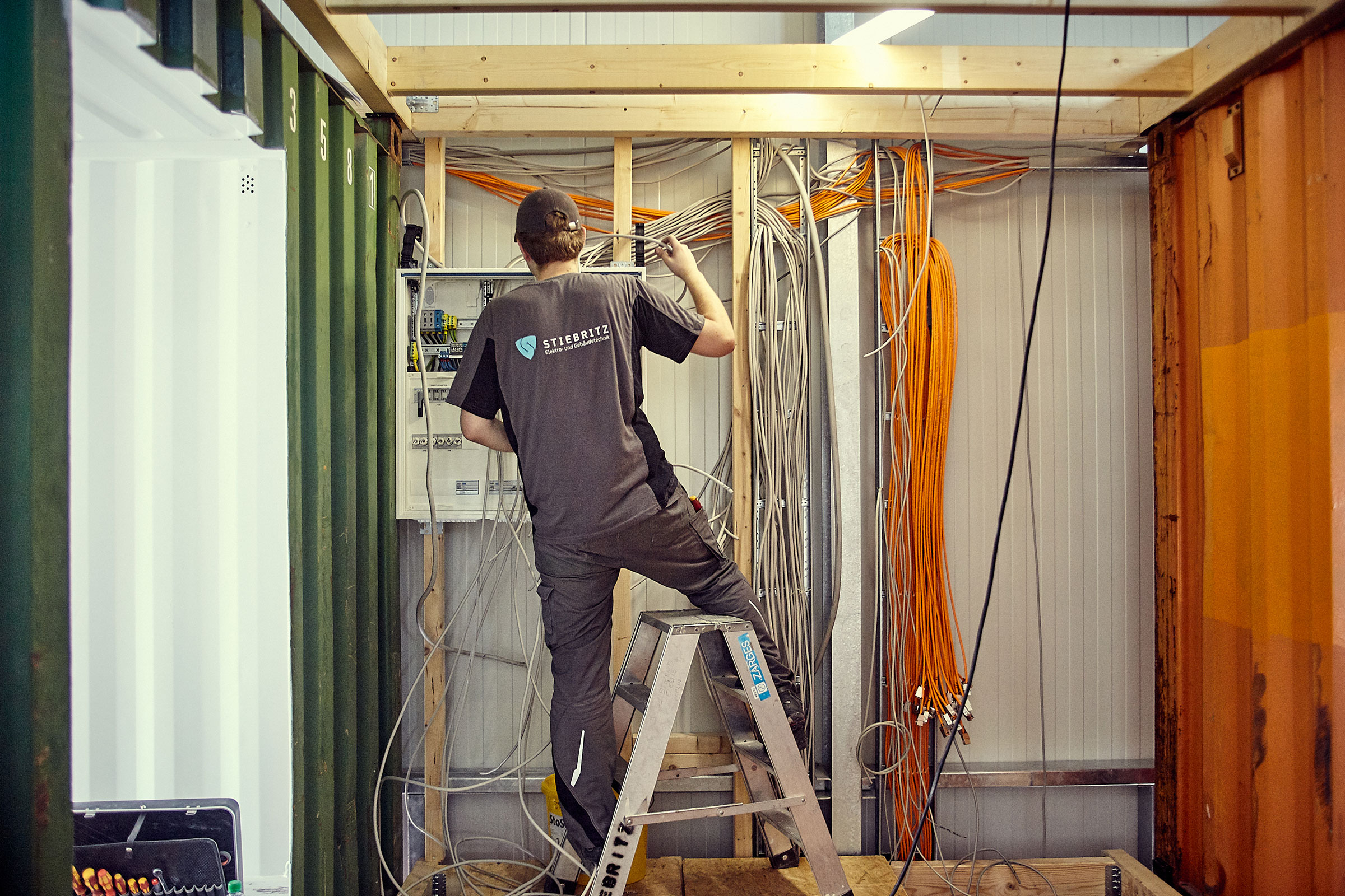 Elektriker på en stege som installerar elektriska ledningar i en container