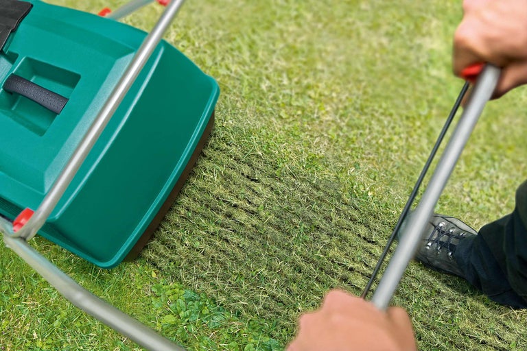 En gräsmattluftare skjuts över en gräsmatta och luftar den.