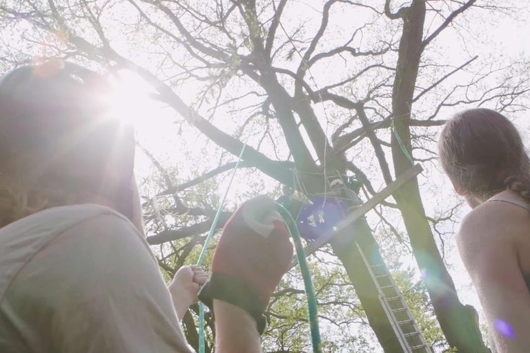 Personer bygger ett trädkoja med en stege och rep.