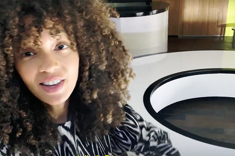 Interiörbild av en kvinna med lockigt hår och mönstrad topp framför ett vitt bord.