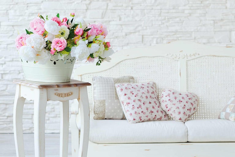 Dekorativ scen med blombukett i en hink på ett sidobord bredvid en soffa med kuddar