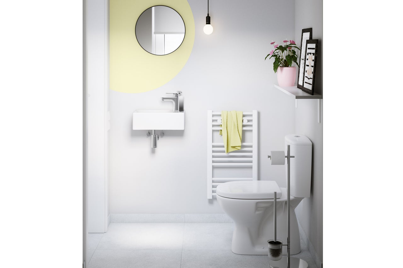 Ljus, modern gästtoalett med litet vägghängt tvättställ, rund spegel, vit handdukstork och golvstående toalett.