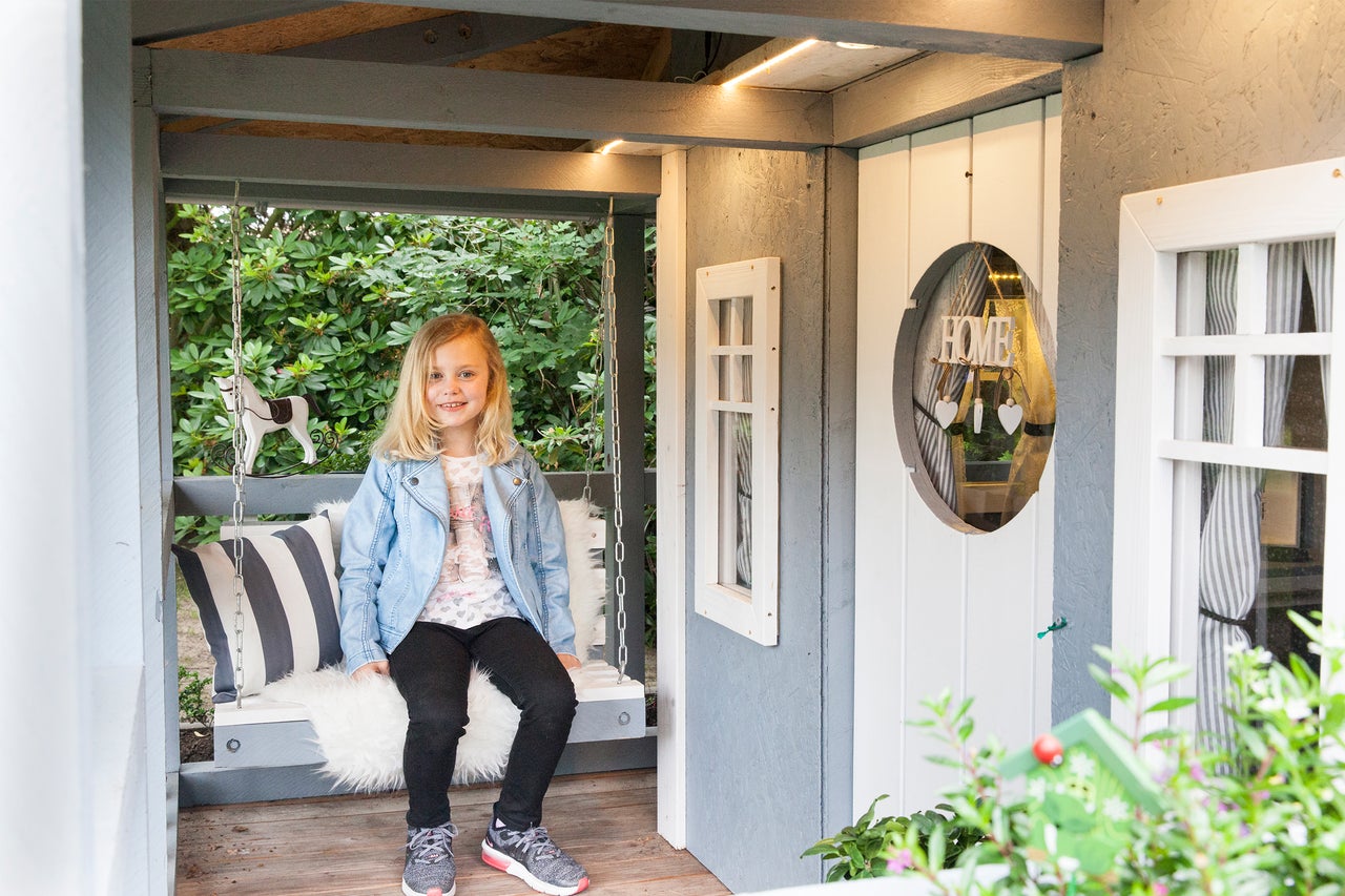 Flicka sitter på en gunga i en lekstuga med kuddar och dekorationer