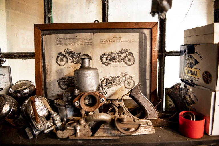 Verkstadsscen i vintagestil med verktyg, motorcykeldelar och en bok med motorcykelritningar