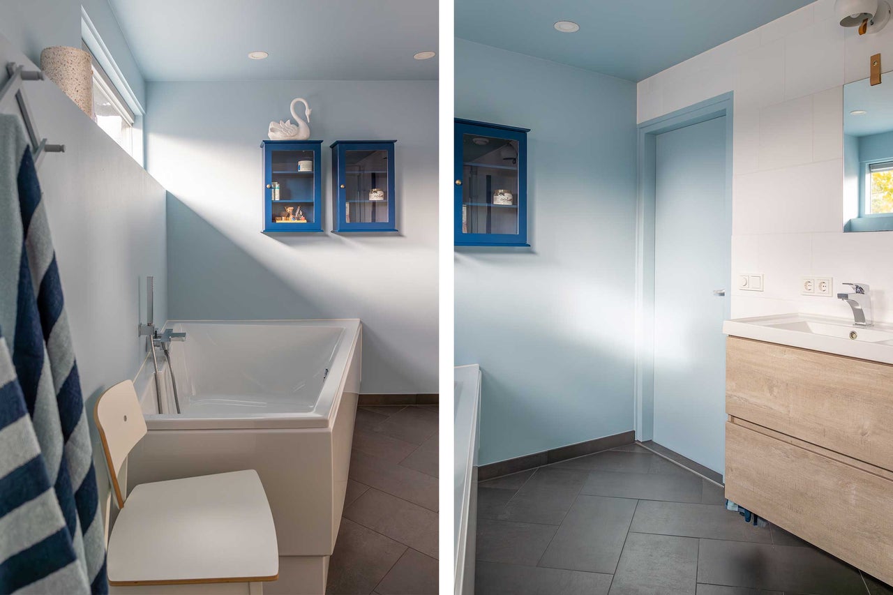 Badrum med badkar, tvättställsskåp, blå väggskåp och sittplats