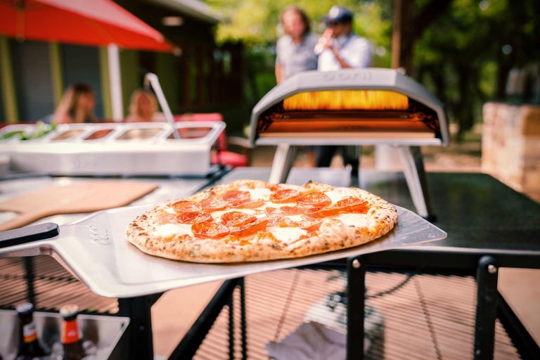 Pizza med salami på pizzaspade framför pizzaugn