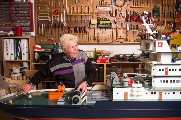 En man bygger en fartygsmodell i en verkstad med verktyg.