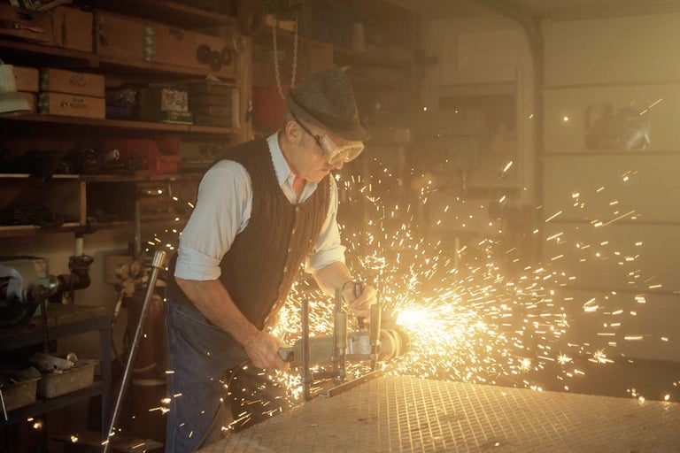 En man med skyddsglasögon bearbetar metall med en vinkelslip, vilket skapar gnistor.