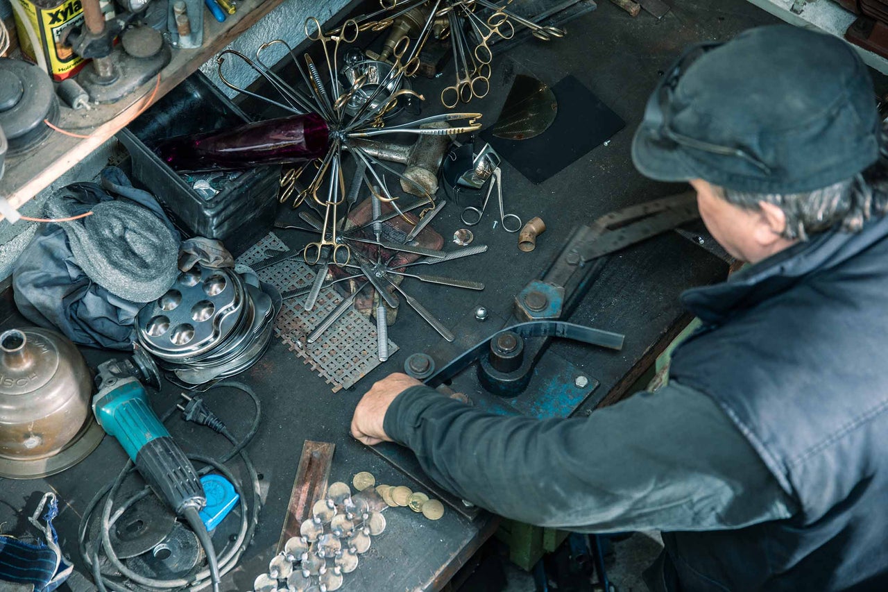 Arbetsbänksvy med verktyg, metalldelar och en person som böjer metall