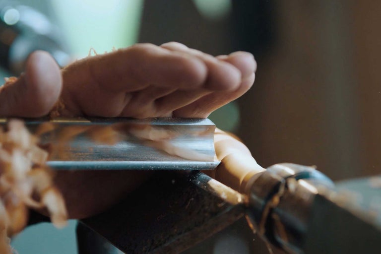 Närbild av en hand som håller ett svarvjärn när man svarvar en träbit.