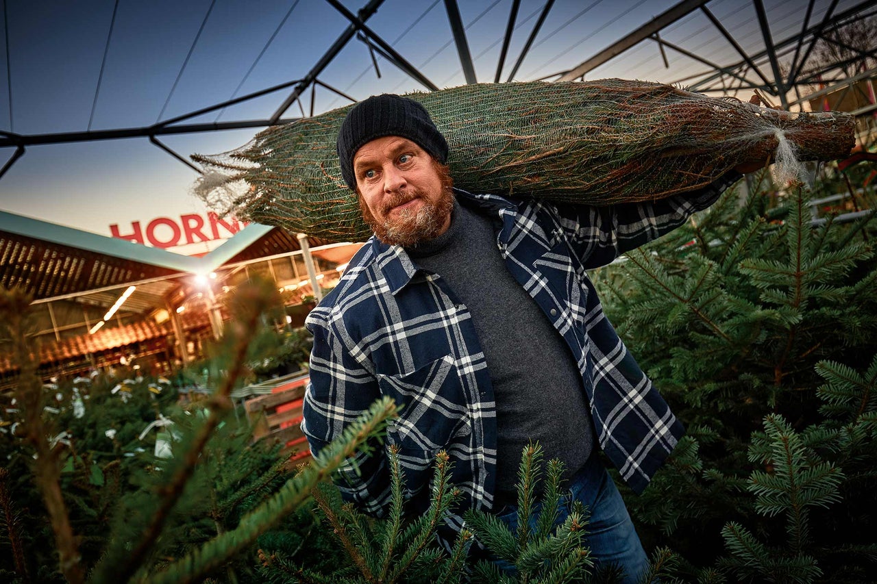 En man bär en förpackad julgran på axeln i en Hornbach-butik.