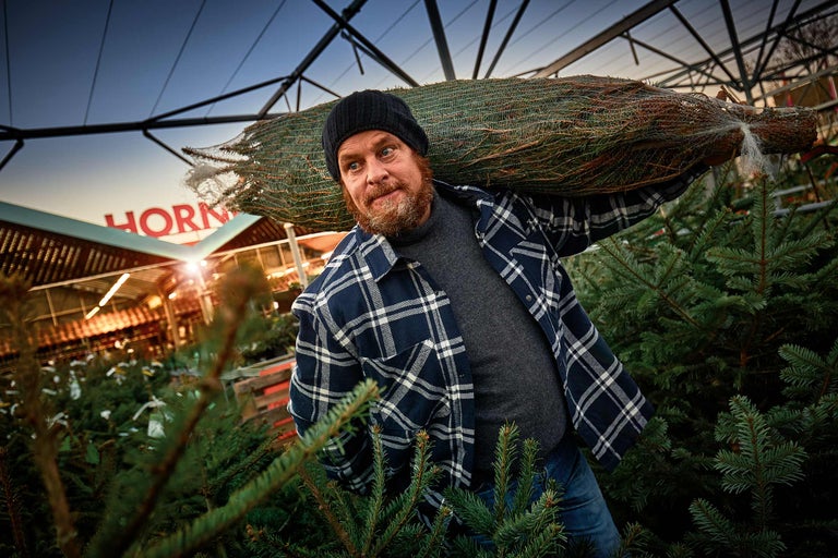 En man bär en förpackad julgran på axeln i en Hornbach-butik.