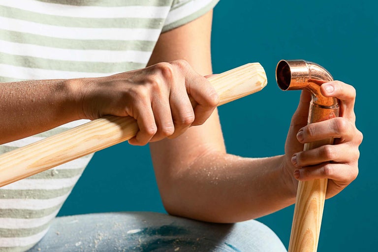 En person håller ett kopparrör och en träpinne.