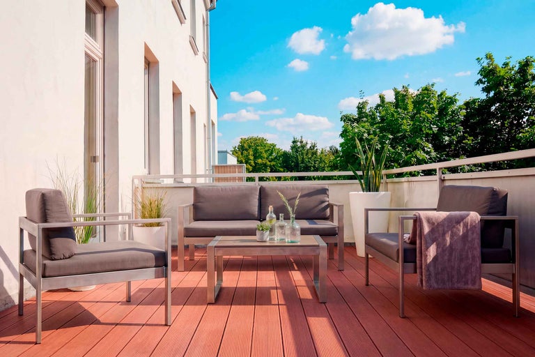Modern loungeset i metall med grå dynor på en terrass med WPC-trall, bestående av soffa, fåtöljer och bord.