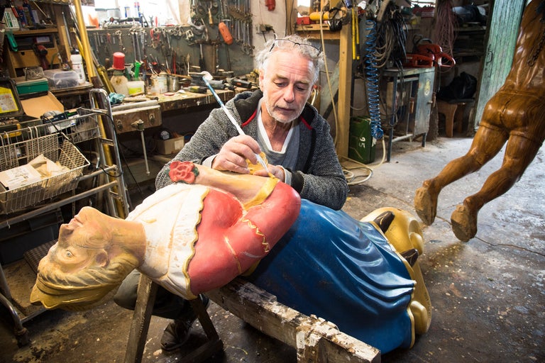 En hantverkare restaurerar en träfigur med en pensel i en verkstad.