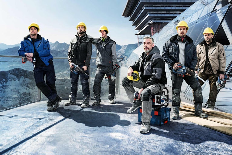 Grupp av byggnadsarbetare med verktyg och skyddskläder framför ett byggprojekt