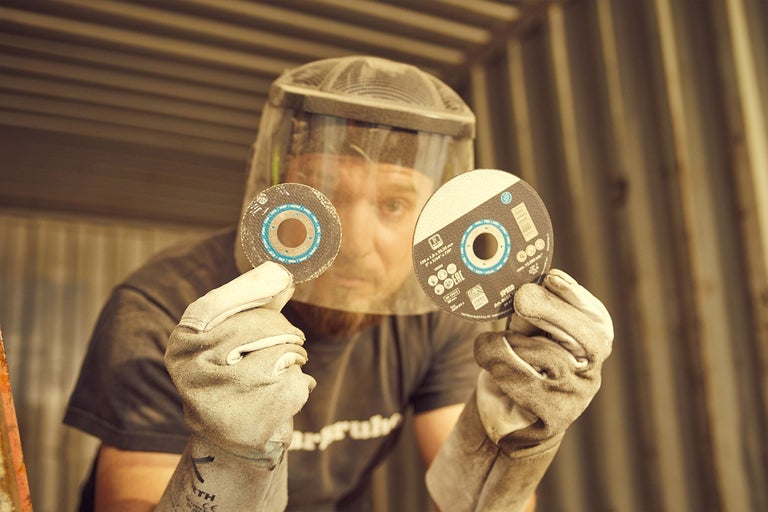 Man med ansiktsskydd och arbetshandskar håller två kapskivor i handen.