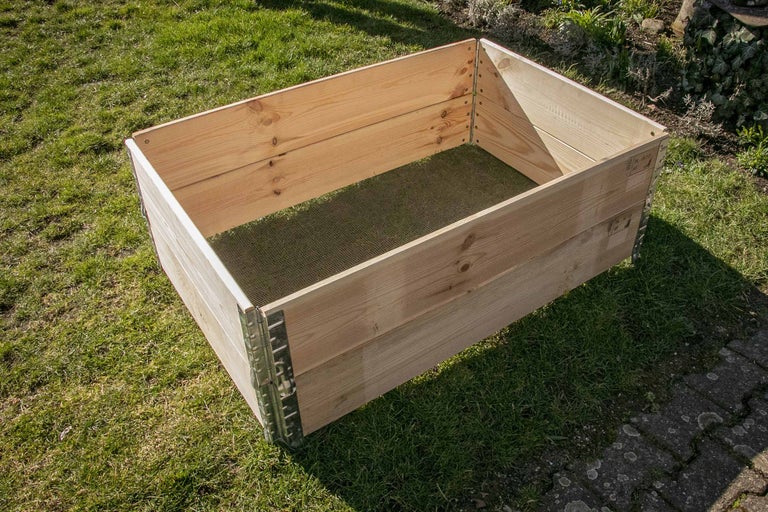 Trädgårdshögbädd i trä med metallhörn på en gräsmatta