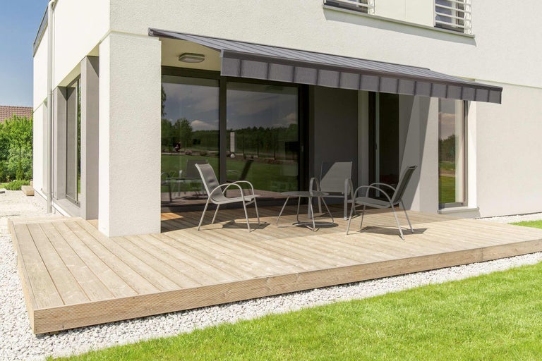 Terrass med markis, trädgårdsmöbler och trägolv framför ett bostadshus