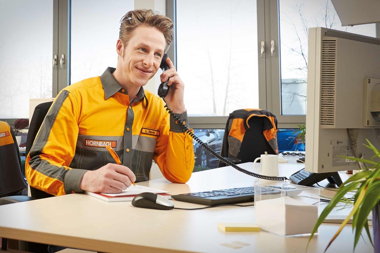 En Hornbach-anställd ringer och gör anteckningar vid sitt skrivbord.
