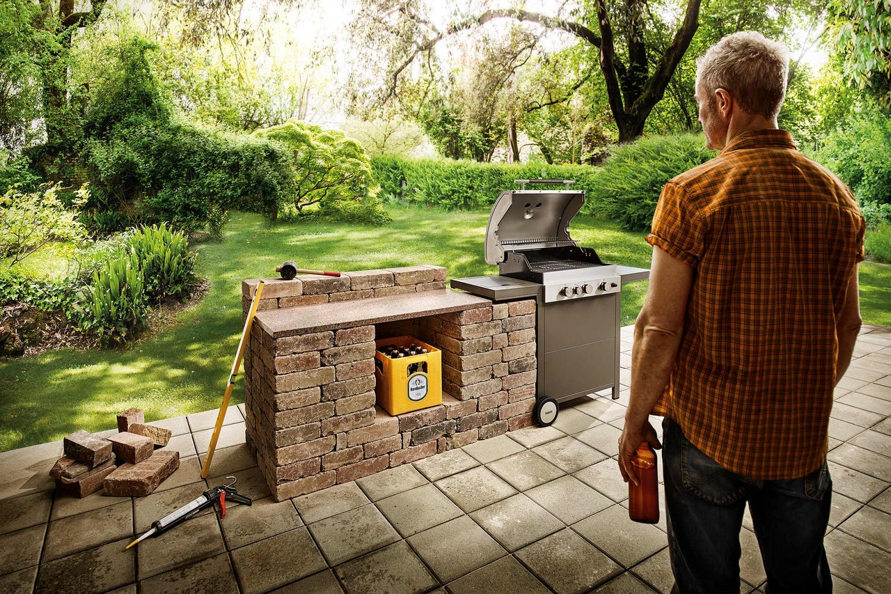 Trädgårdsscen med grill, ölbricka, stenar och verktyg på stenterrass