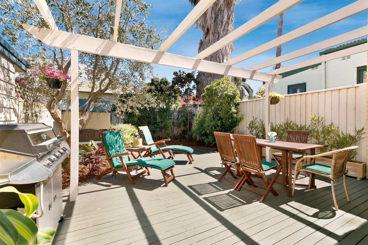 Terrass med grill, träbord, stolar och solstolar under en pergola