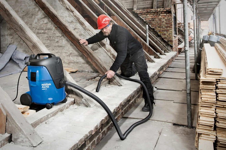 En arbetare använder en våt- och dammsugare från Nilfisk Alto för att rengöra en byggarbetsplats.