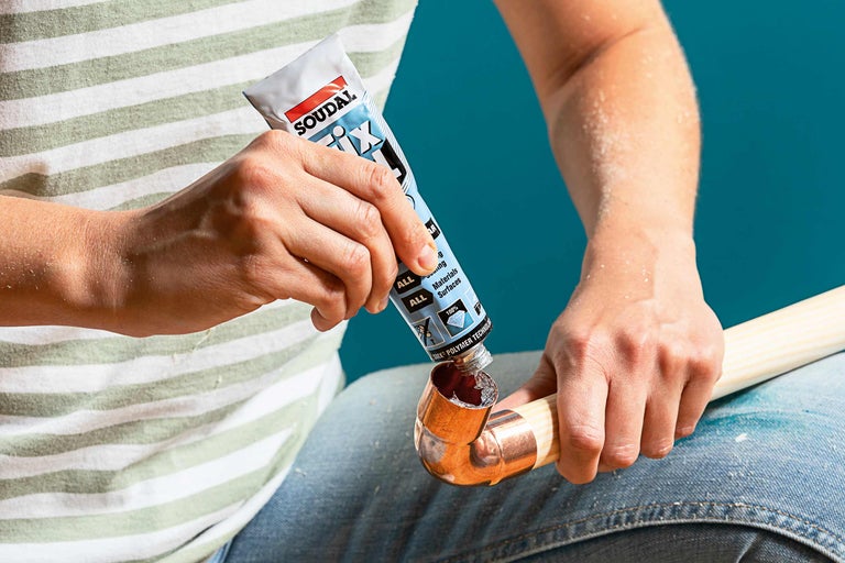 En person applicerar lim från en Soudal Fix All tub på ett kopparrör