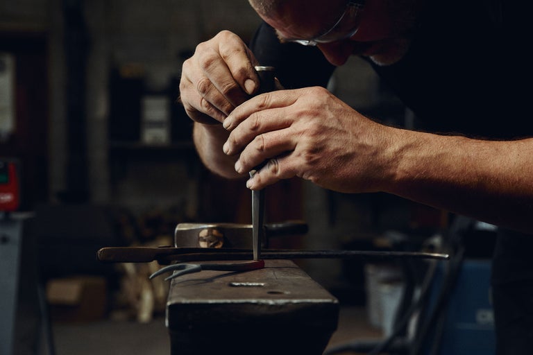 Smed bearbetar glödande metall med en mejsel på ett städ