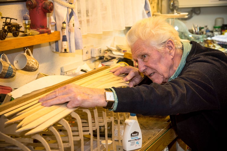 Man arbetar på en fartygsmodell med träribbor och lim.