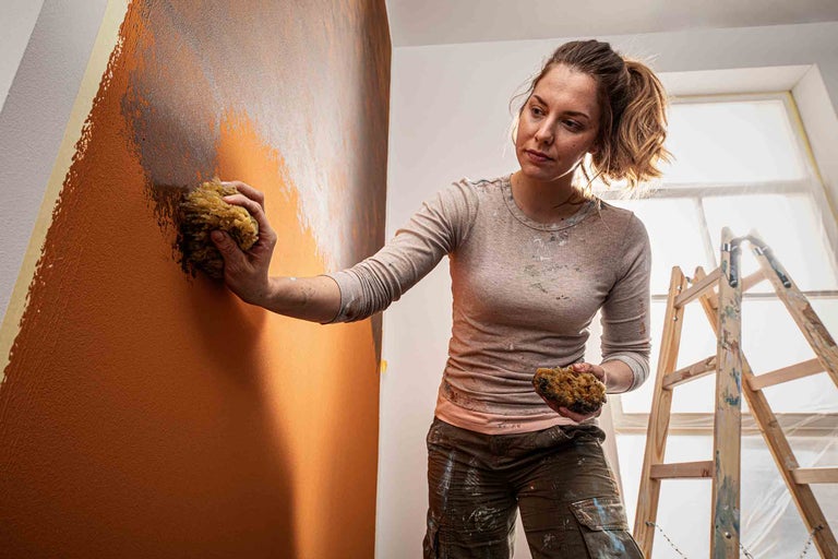 Kvinna dekorerar vägg med svamp och färg, inklusive stege i rummet