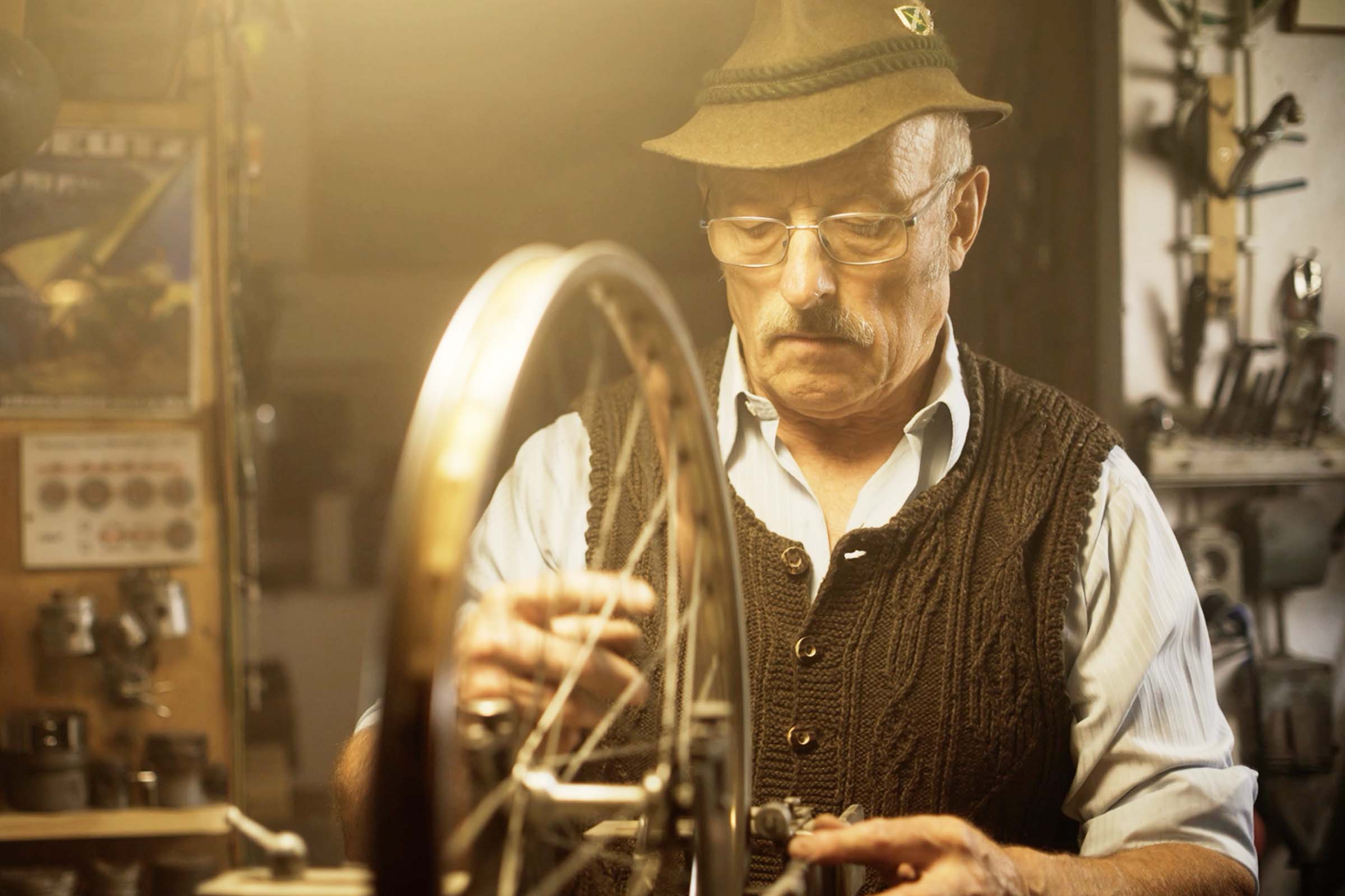 En man med hatt reparerar en cykel i en verkstad.