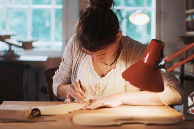 En kvinna bearbetar en träbit med ett verktyg vid ett bord.