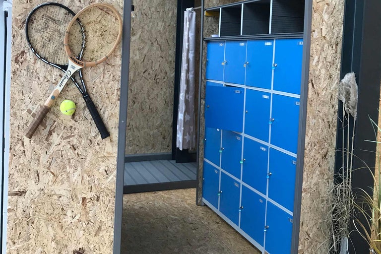 Interiör med blå skåp, omklädningsrum med gardin, två tennisracketar och en tennisboll