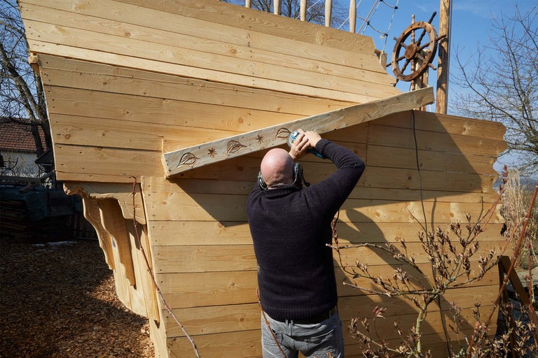 Man bearbetar trä på ett lekfartyg med en vinkelslip
