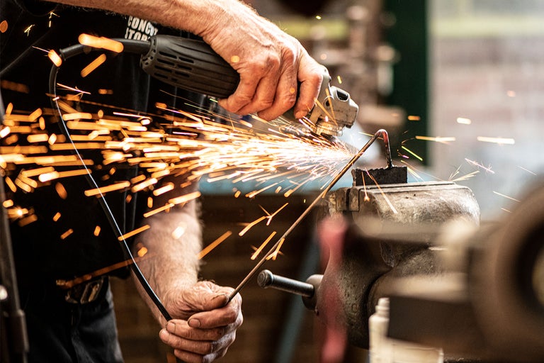 En person slipar en metallbit med en slipmaskin, gnistor sprutar.