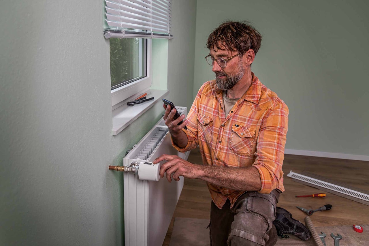 Man installerar en digital radiatortermostat och använder en smartphone för att styra den.