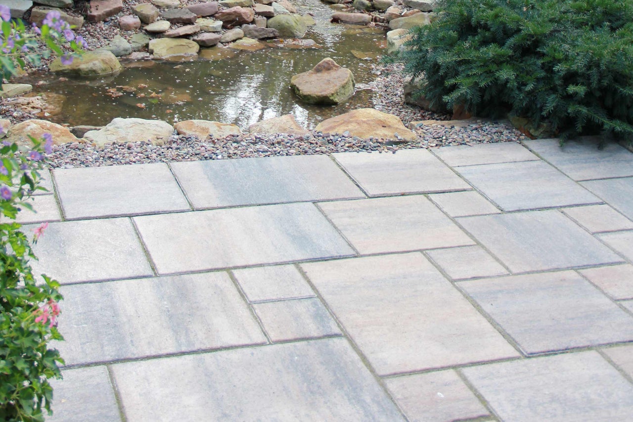 Trädgårdslandskap med damm och lagd marksten