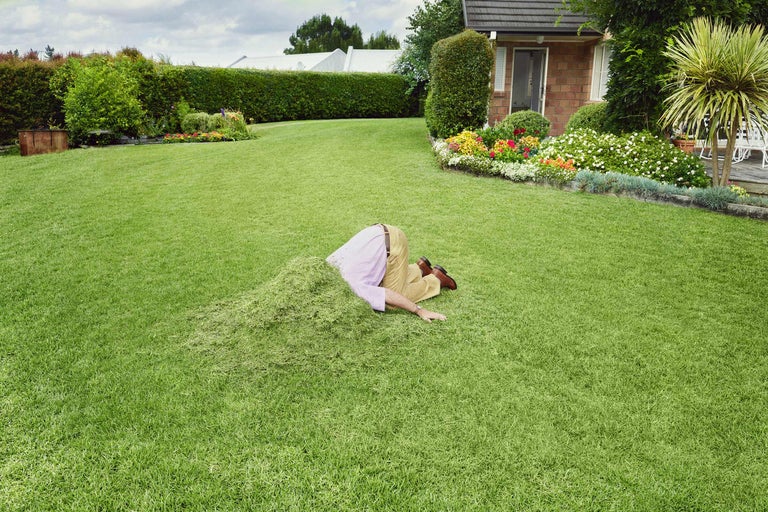 En person har huvudet i en hög med nyklippt gräs i en trädgård.