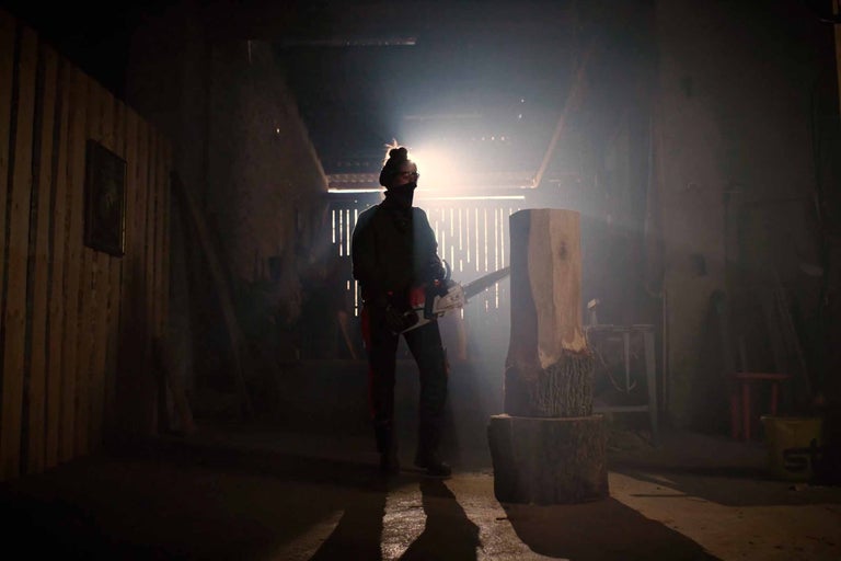 Man med motorsåg som bearbetar en trädstam i ett mörkt rum