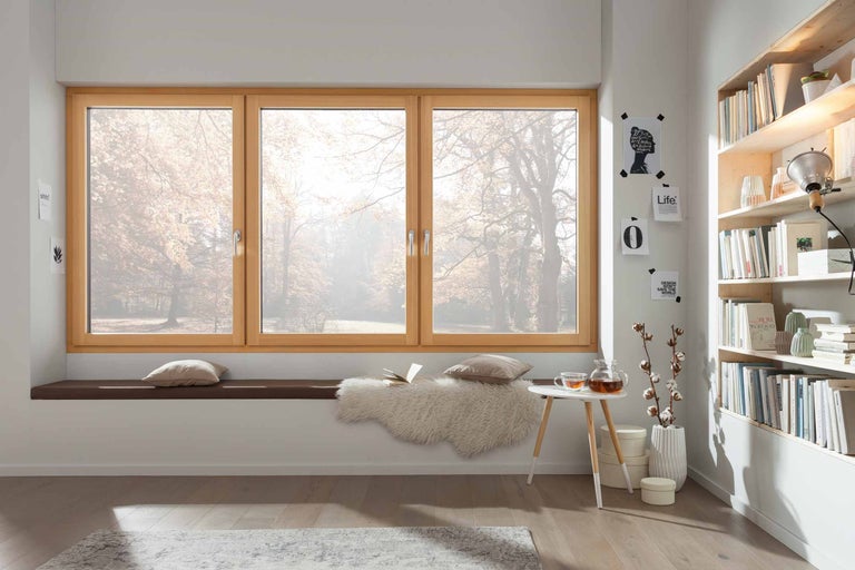 Ljus rumsscen med träfönster, sittbänk, kuddar, tebord och bokhylla för ett mysigt boende.