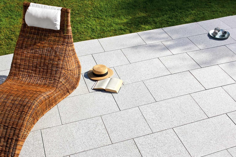 Trädgårdsscen med rottingstol, stenläggning och sommaraccessoarer