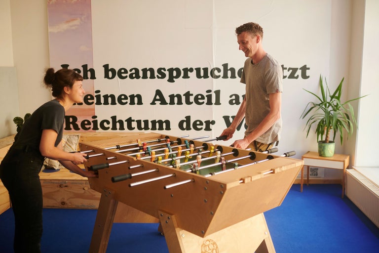 Två personer spelar bordsfotboll i ett ljust rum.